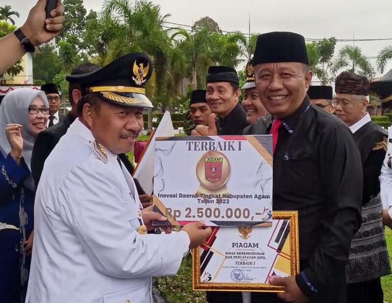 Bupati Agam Andri Warman menyerahkan penghargaan kepada Kepala Disdukcapil Agam Helton. (AMC Agam)