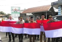 Bupati Pasbar, Yulianto, Wakil Bupati M. Ihpan, unsur Forkopimda, pejabat instansi vertikal dan OPD membagikan Bendera Merah Putih kepada Masyarakat, Senin (11/8/2025). (Foto: Diskominfo Pasbar)