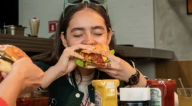 Ilustrasi seorang wanita makan burger. (Foto: Pexels)