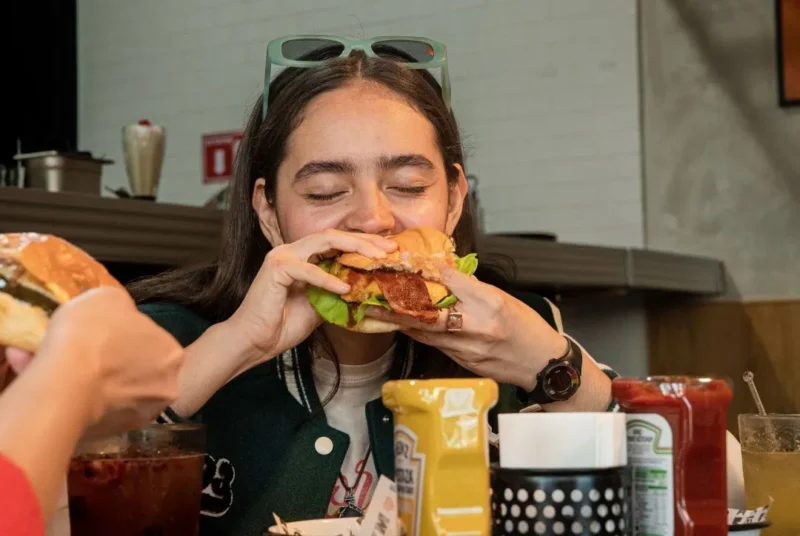 Ilustrasi seorang wanita makan burger. (Foto: Pexels)