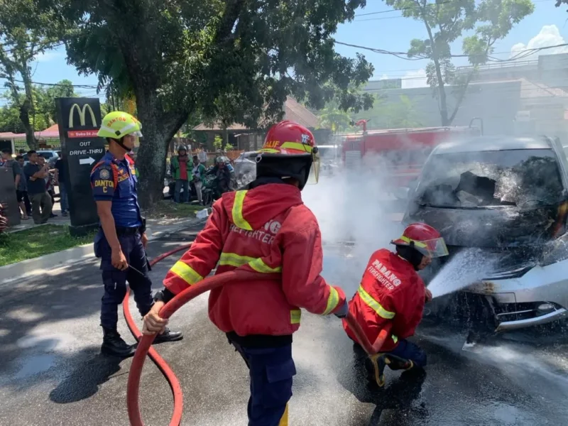 Petugas Damkar Padang memadamkan api yang membakar mobil Honda Freed di depan McDonald's Ahmad Yani Padang, Jumat (24/7/2026). (Foto: Dinas Damkar Padang)