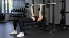 Ilustrasi seorang wanita melakukan latihan bench press di pusat kebugaran. (Foto: AI Generate)