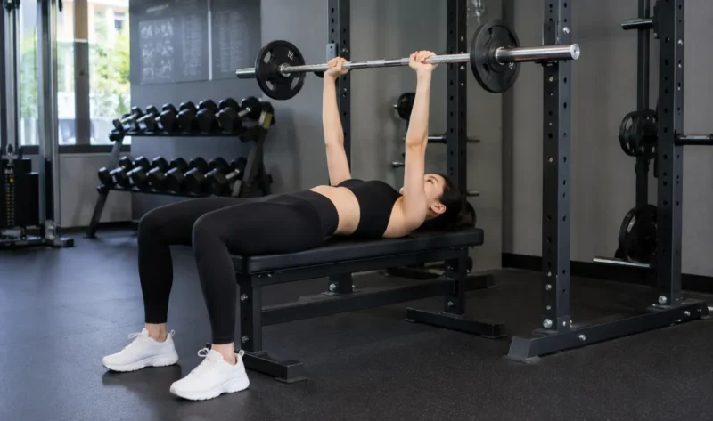Ilustrasi seorang wanita melakukan latihan bench press di pusat kebugaran. (Foto: AI Generate)