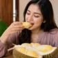 Ilustrasi seorang wanita sedang menyantap durian. (Foto: AI Generated)