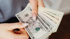 Ilustrasi seorang wanita memegang uang dolar AS. (Foto: Pexels)
