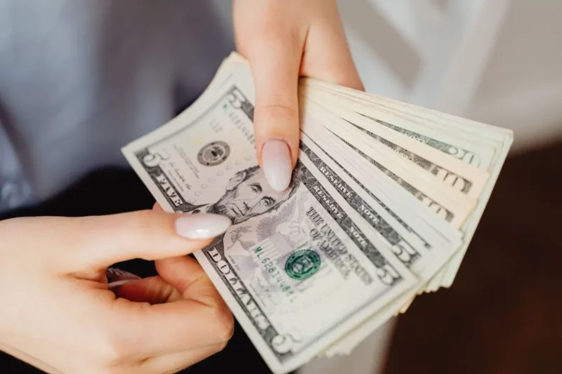 Ilustrasi seorang wanita memegang uang dolar AS. (Foto: Pexels)
